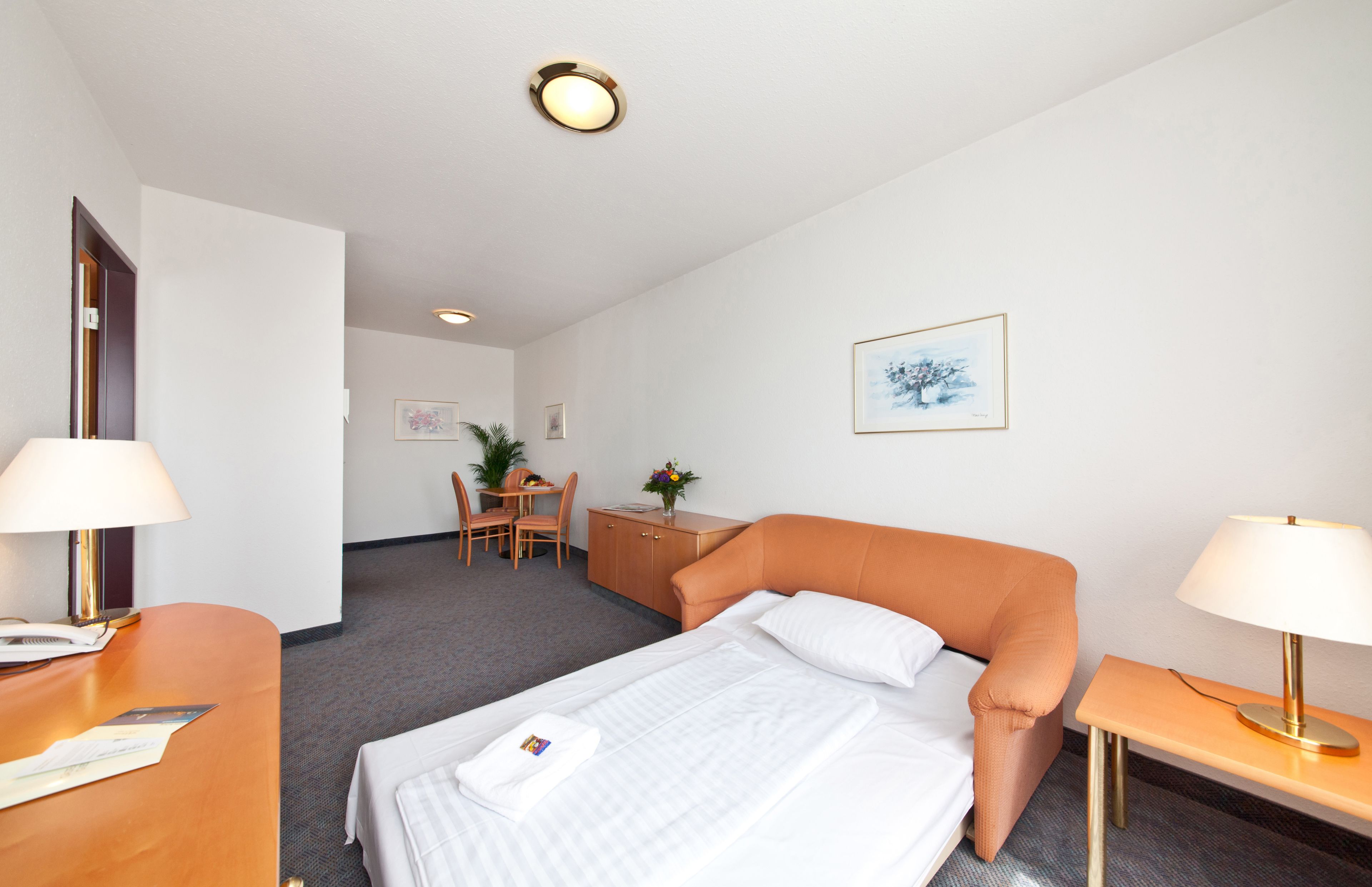 Une chambre d’hôtel comprenant un lit, un bureau, une chaise, une petite table et une table de chevet.