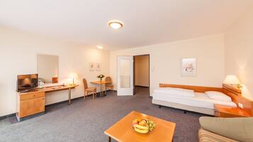 A hotel room with a bed, a desk with a computer, a chair, a small table with fruit, and a sofa.