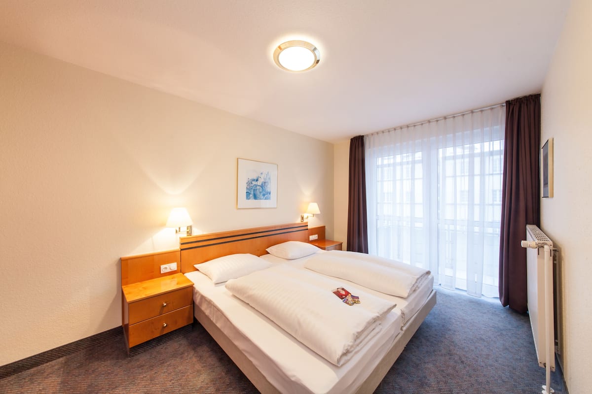 A hotel room with a large bed, bedside lamps, a nightstand, a framed picture on the wall, and a window with curtains.