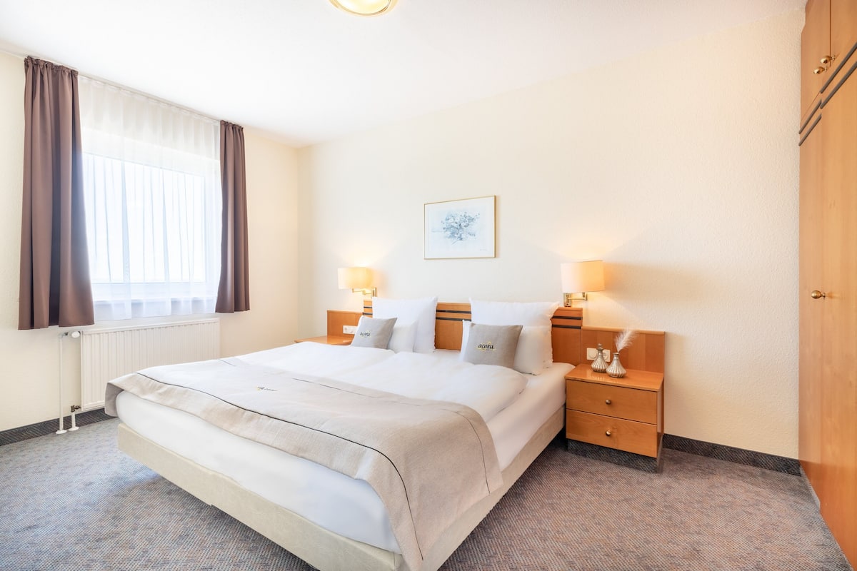A hotel room with a large bed, two bedside tables with lamps, a wooden wardrobe, and a window with curtains.