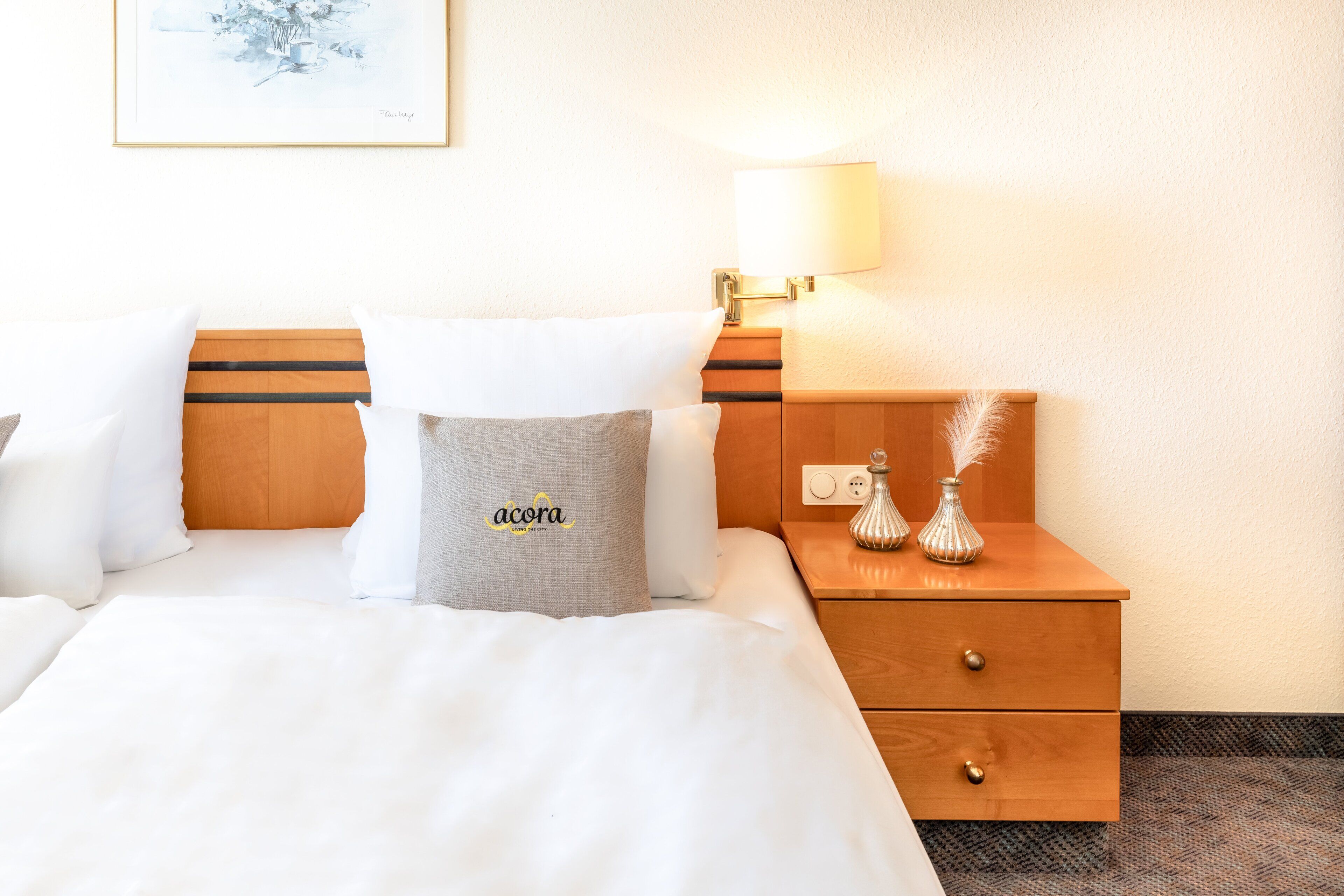 Habitació d'hotel amb un llit, una nitòria, una làmpada i un vas petit amb plomes.