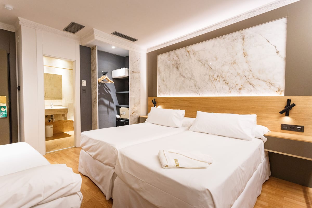 A hotel room with two beds, a marble headboard, a wooden nightstand, and a bathroom visible through an open door.