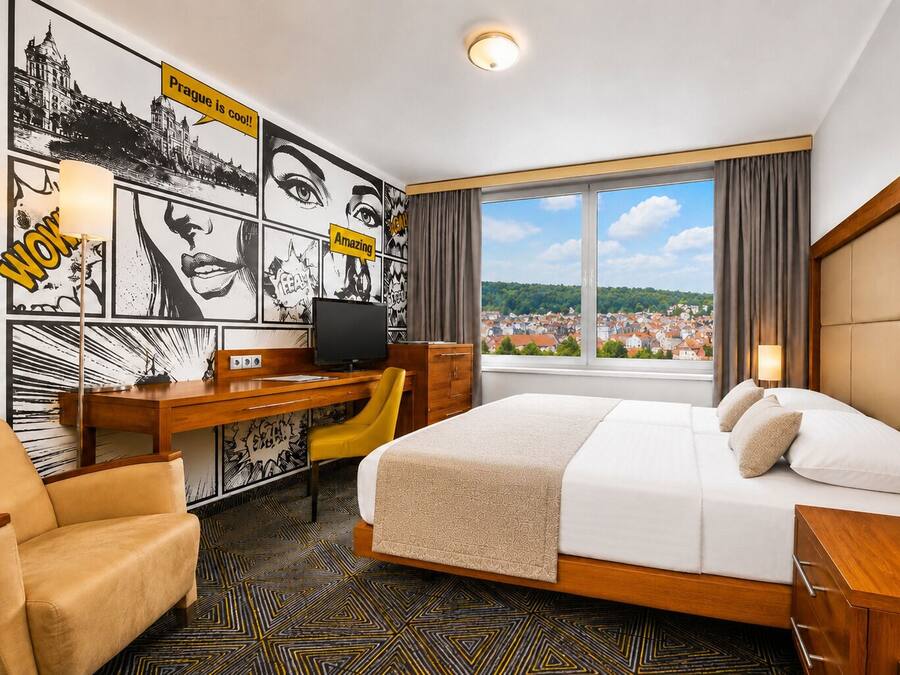 Ein Hotelzimmer mit Bett, Schreibtisch, Stuhl und einem großen Fenster mit Blick auf die Stadt.