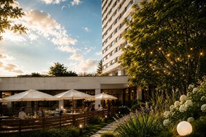 An outdoor dining area with umbrellas, tables, and chairs, surrounded by greenery and a building. - Hotel Uno Prague (Prague)