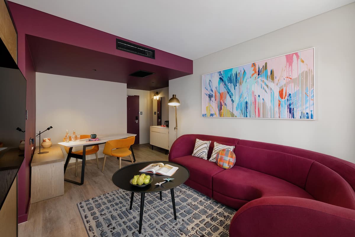 A modern living room with a red sofa, a dining area with orange chairs, and a large abstract painting on the wall.