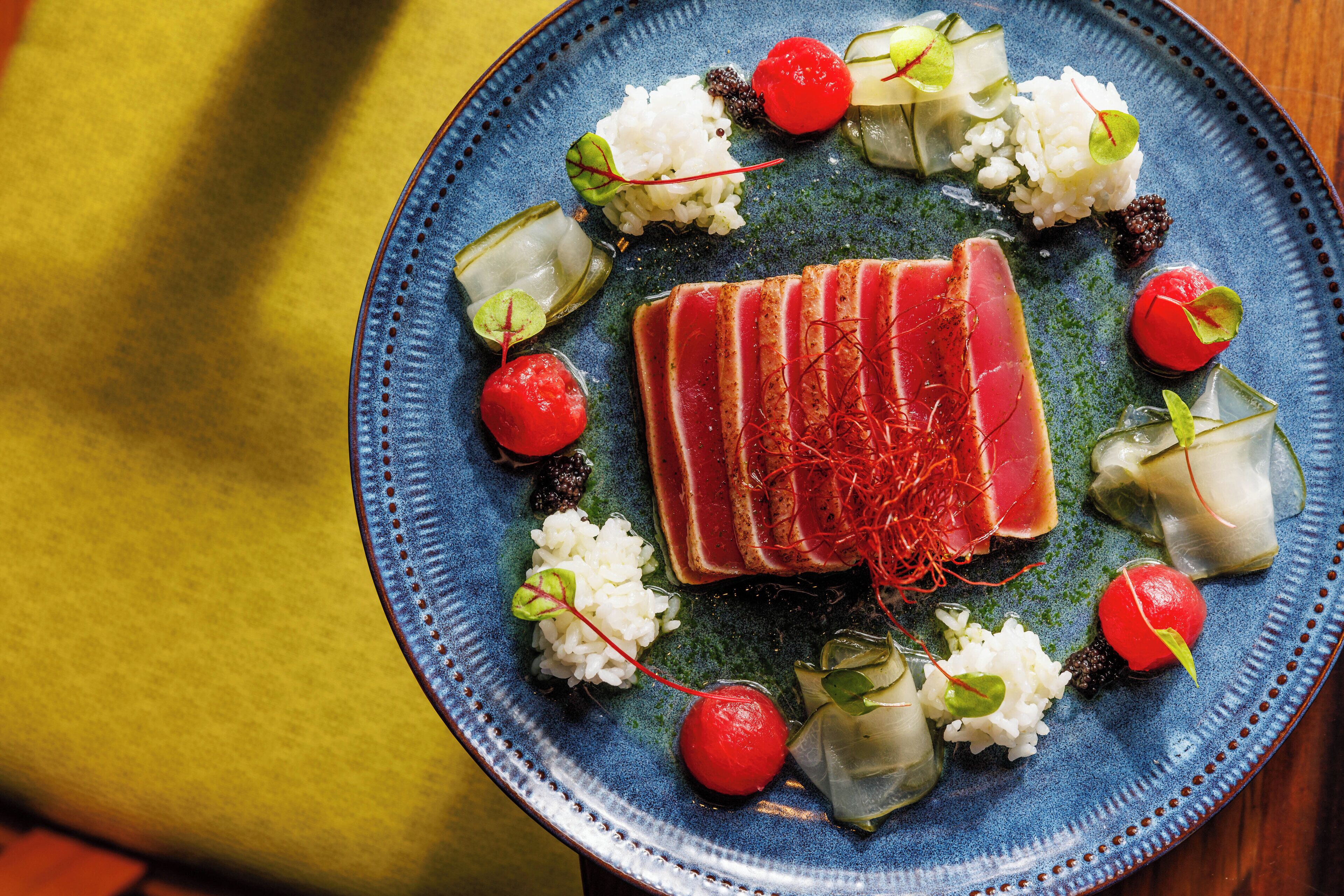 Une assiette bleue contenant des tranches de poisson, du riz et des accompagnements.