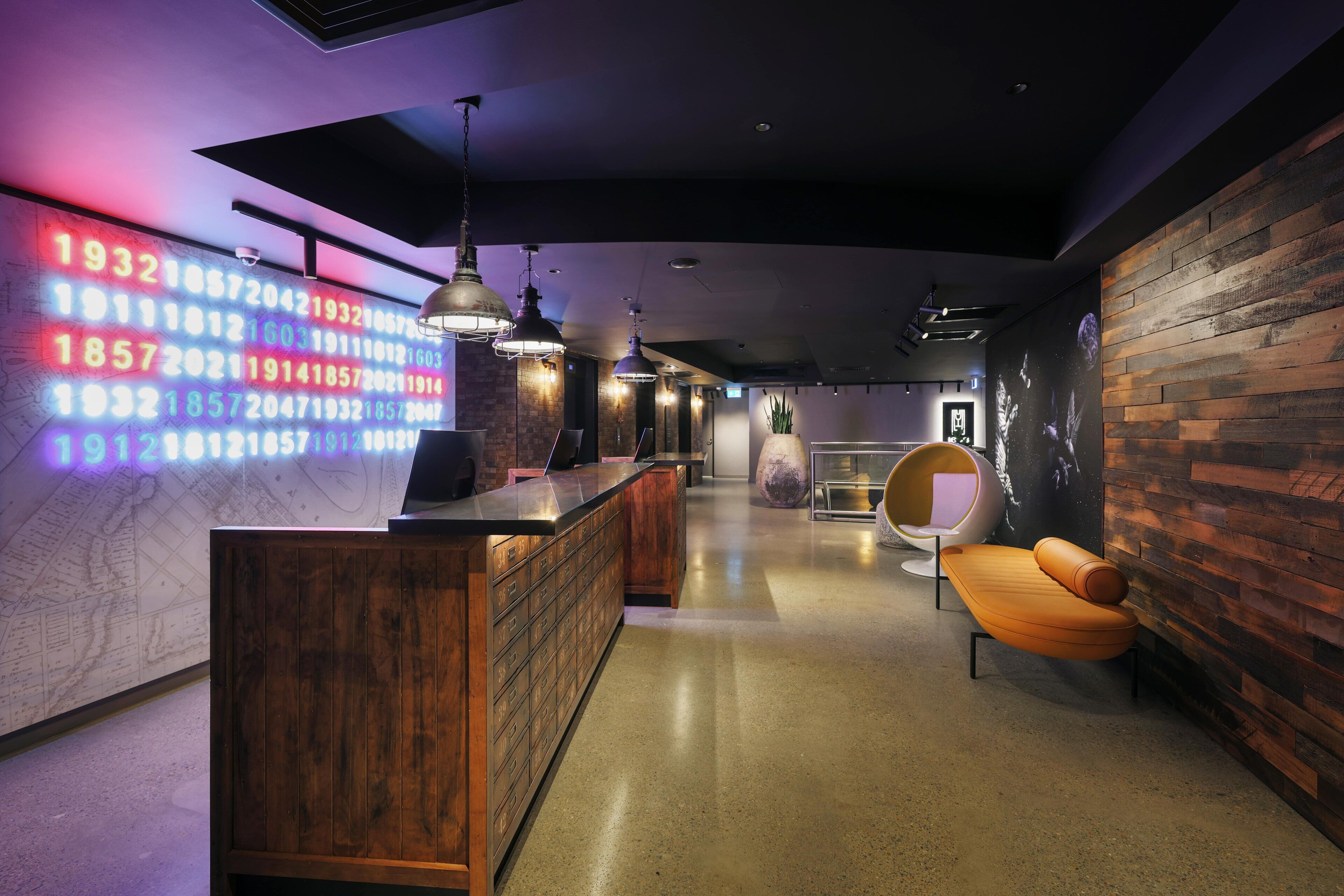 A modern interior with a wooden reception desk, a neon number display, and a seating area with a round chair.