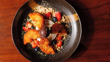 A round, dark-colored plate with a variety of food items including breaded items, strawberries, blueberries, and a dollop of cream.