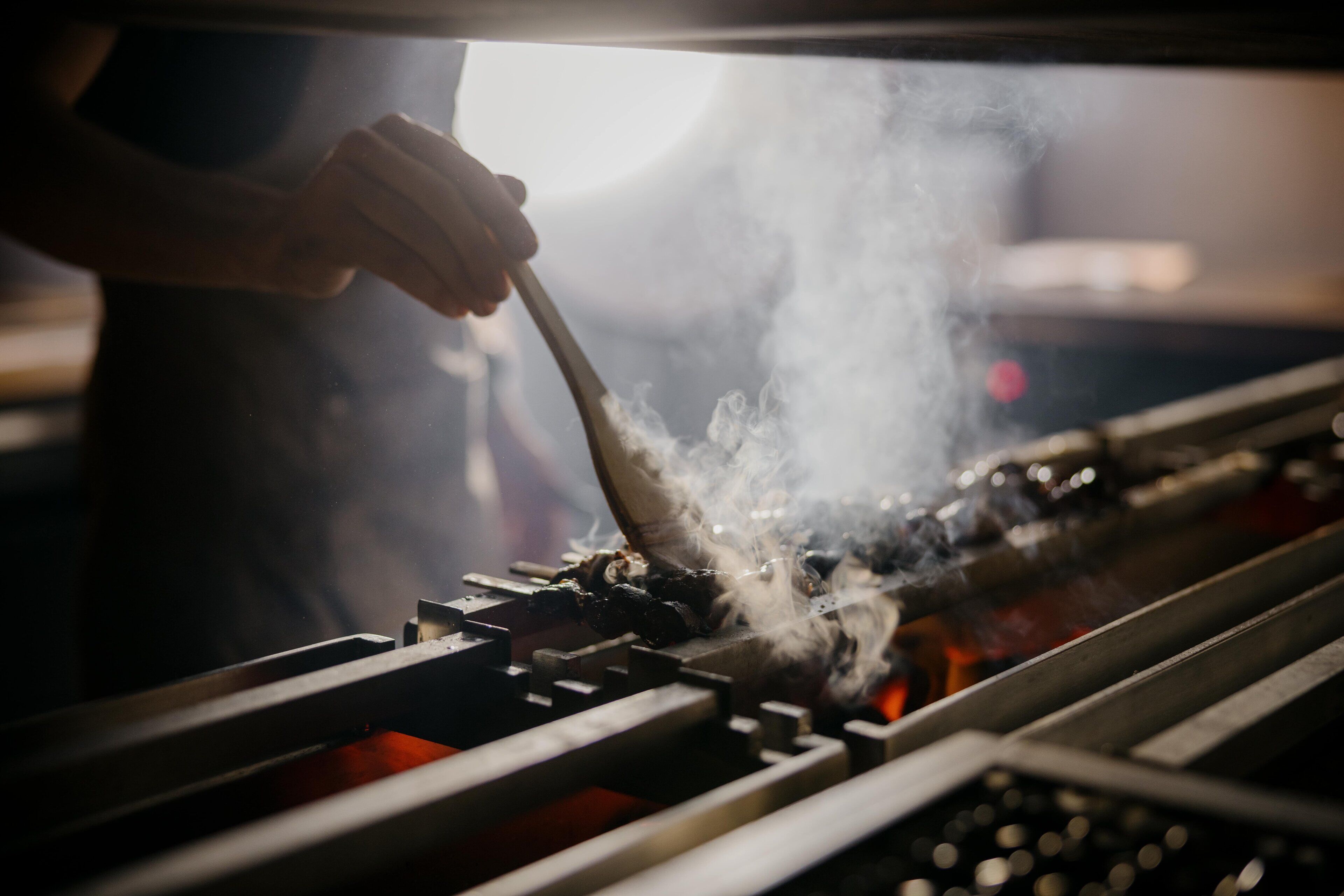 Iemand bereidt eten met een grill, roosterroosters zichtbaar en rook.
