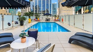 Una piscina interior con sillones de descanso y sombrillas, rodeada de edificios modernos.