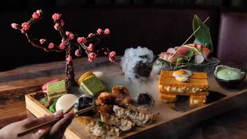 A variety of food items on a wooden tray, including sushi, a dessert, and a decorative branch.