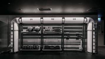 A gym with three workout stations labeled 01, 02, and 03. Each station has different equipment, including kettlebells, a rowing machine, and a cable machine.