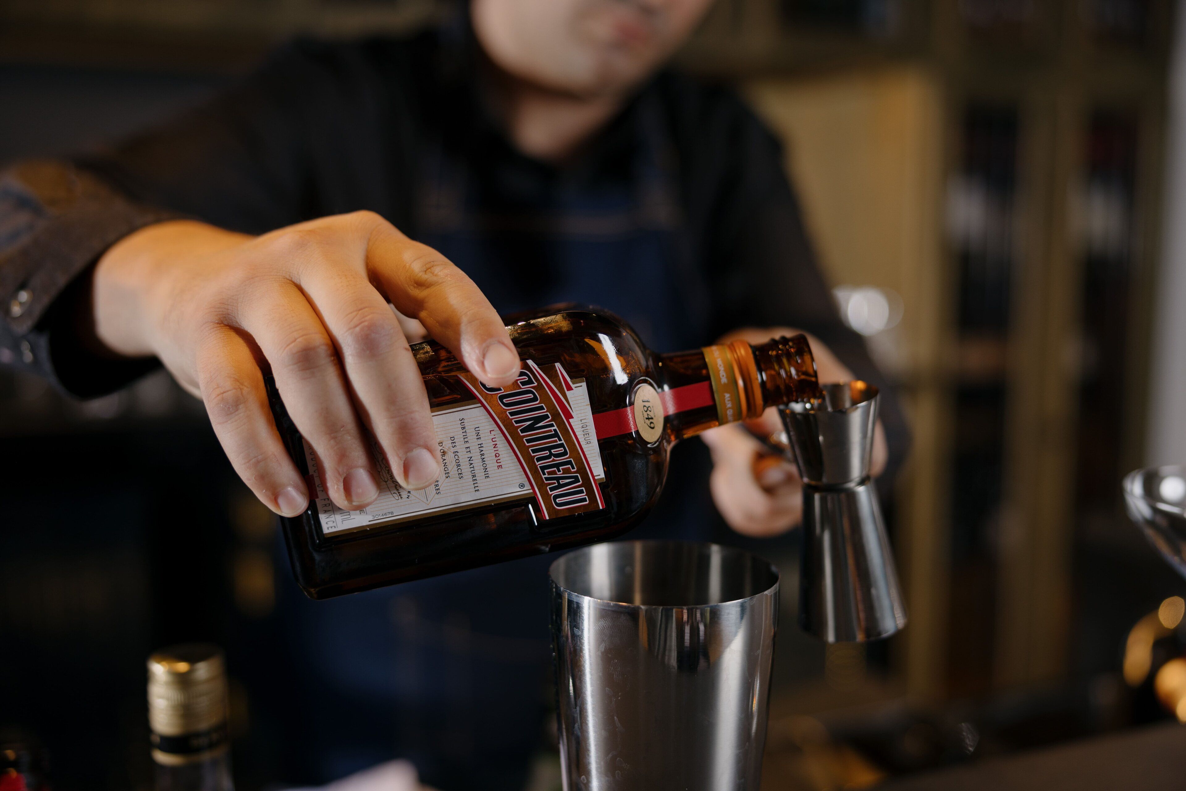 A person pouring a liquid from a bottle into a metal container.