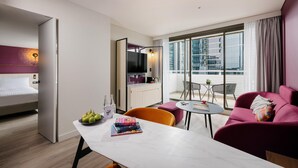 Una habitación de hotel moderna con cama, zona de comedor, sofá y balcón con vistas a la ciudad.