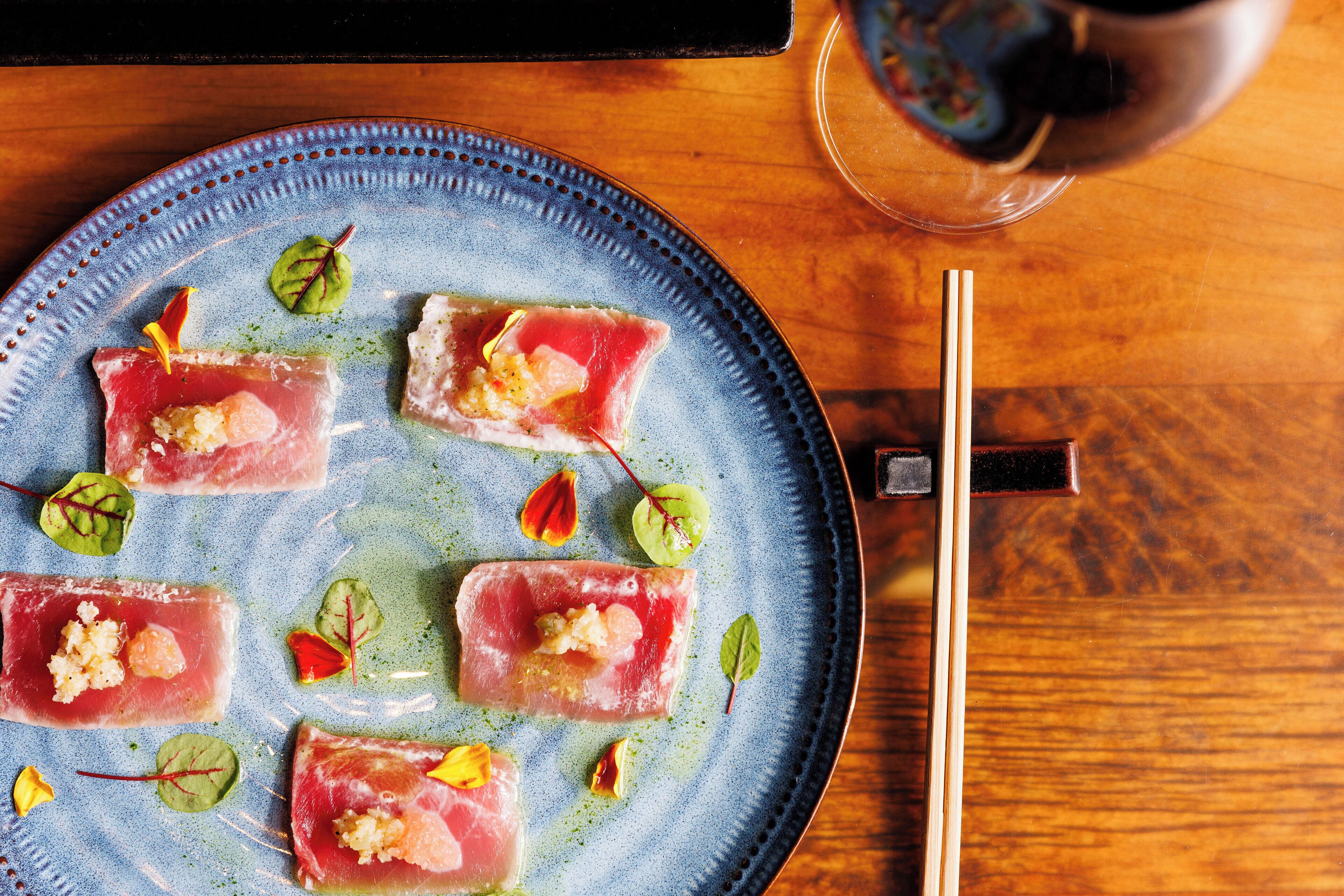 A plate of sashimi with garnishes on a blue ceramic plate.