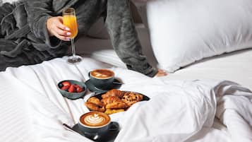 Desayuno con croissants, fresas, café y zumo de naranja sobre una cama.