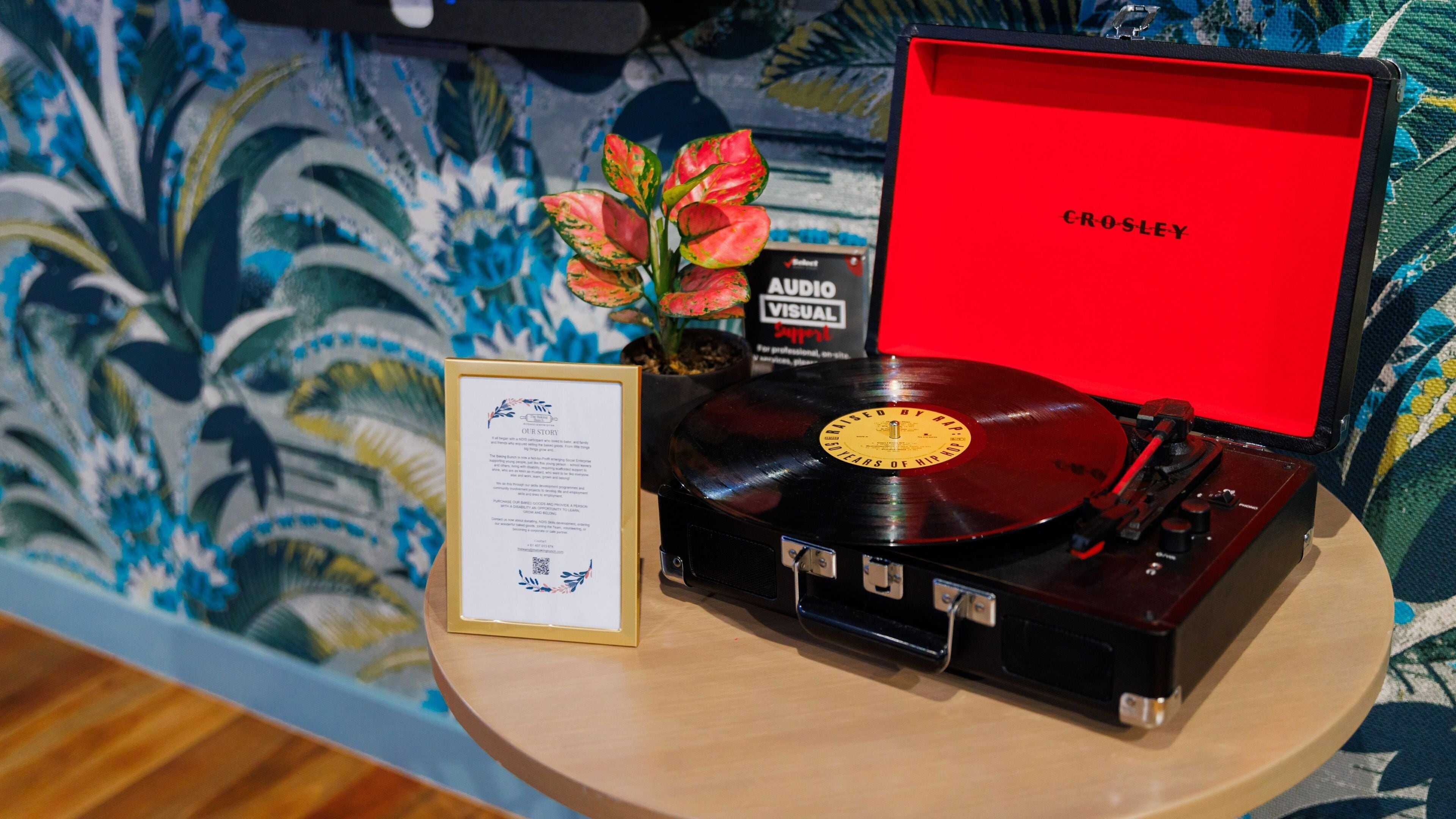 Tocadiscos antiguo con una cubierta roja, un disco de vinilo y una pequeña maceta.