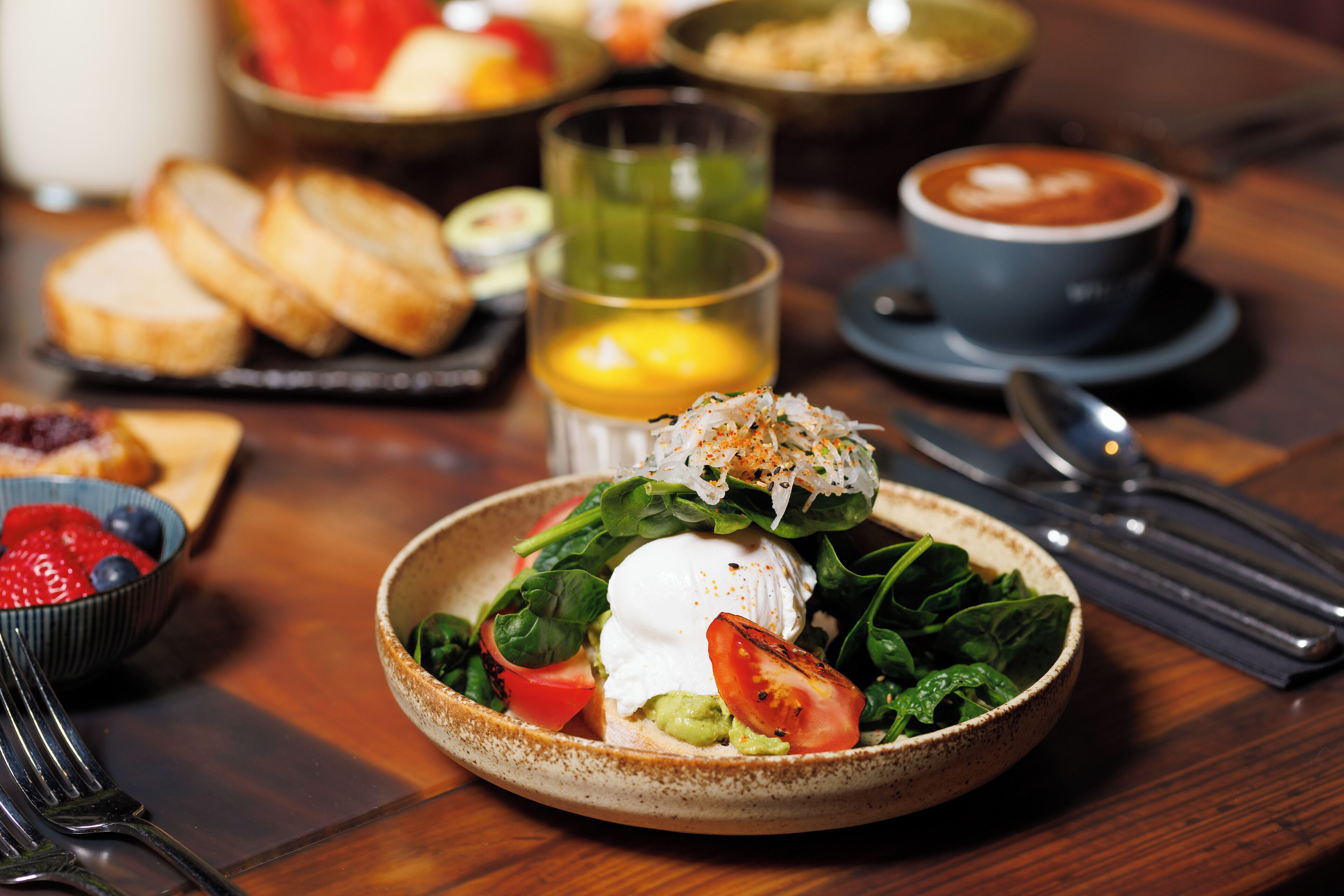 A breakfast setting with a plate of fresh greens, tomatoes, and a poached egg, accompanied by toast and a cup of coffee.
