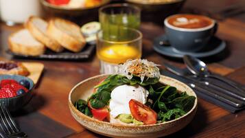 A breakfast setting with a plate of fresh greens, tomatoes, and a poached egg, accompanied by toast and a cup of coffee.
