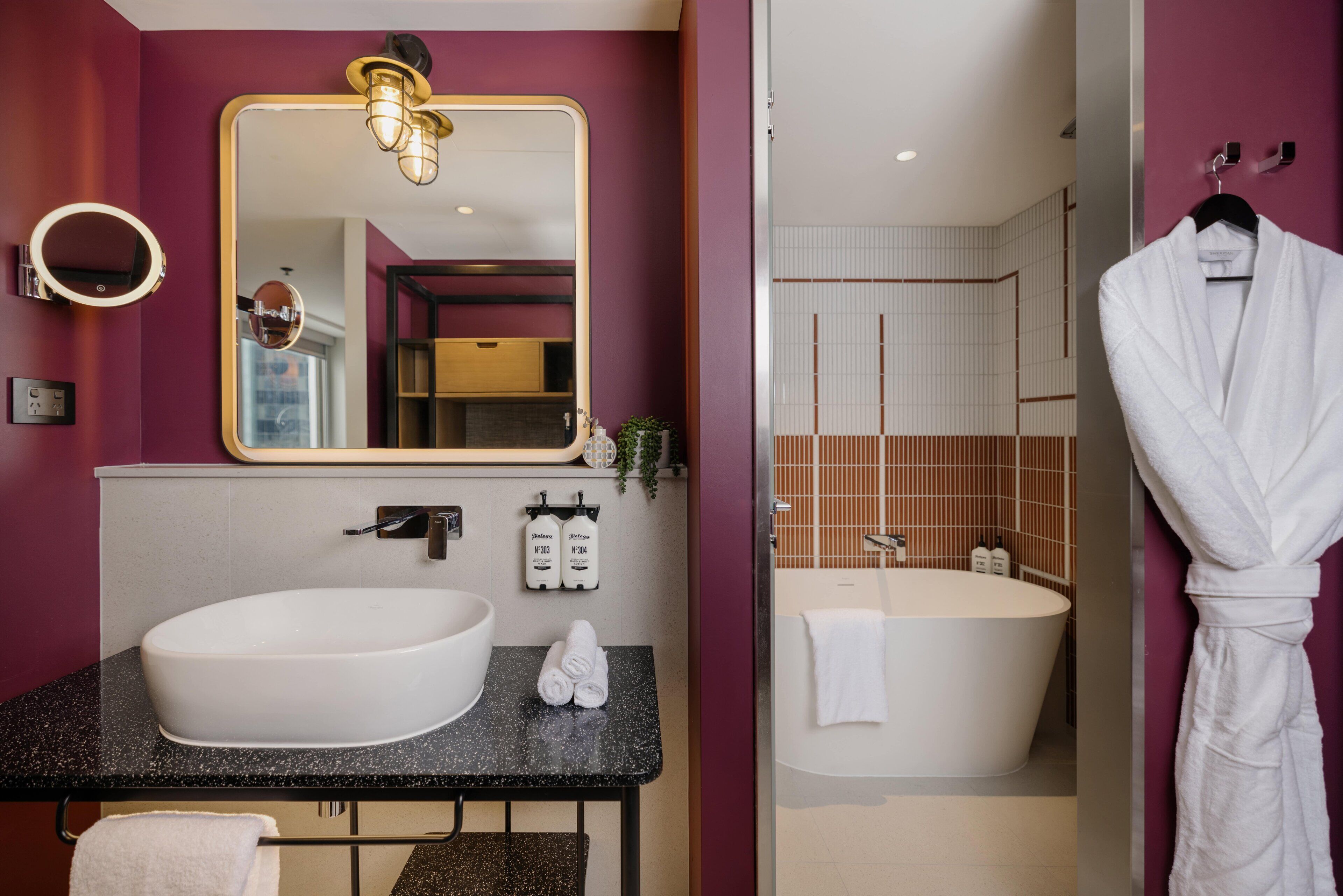 A modern bathroom with a large white sink, a mirror, a round light fixture, and a bathtub.