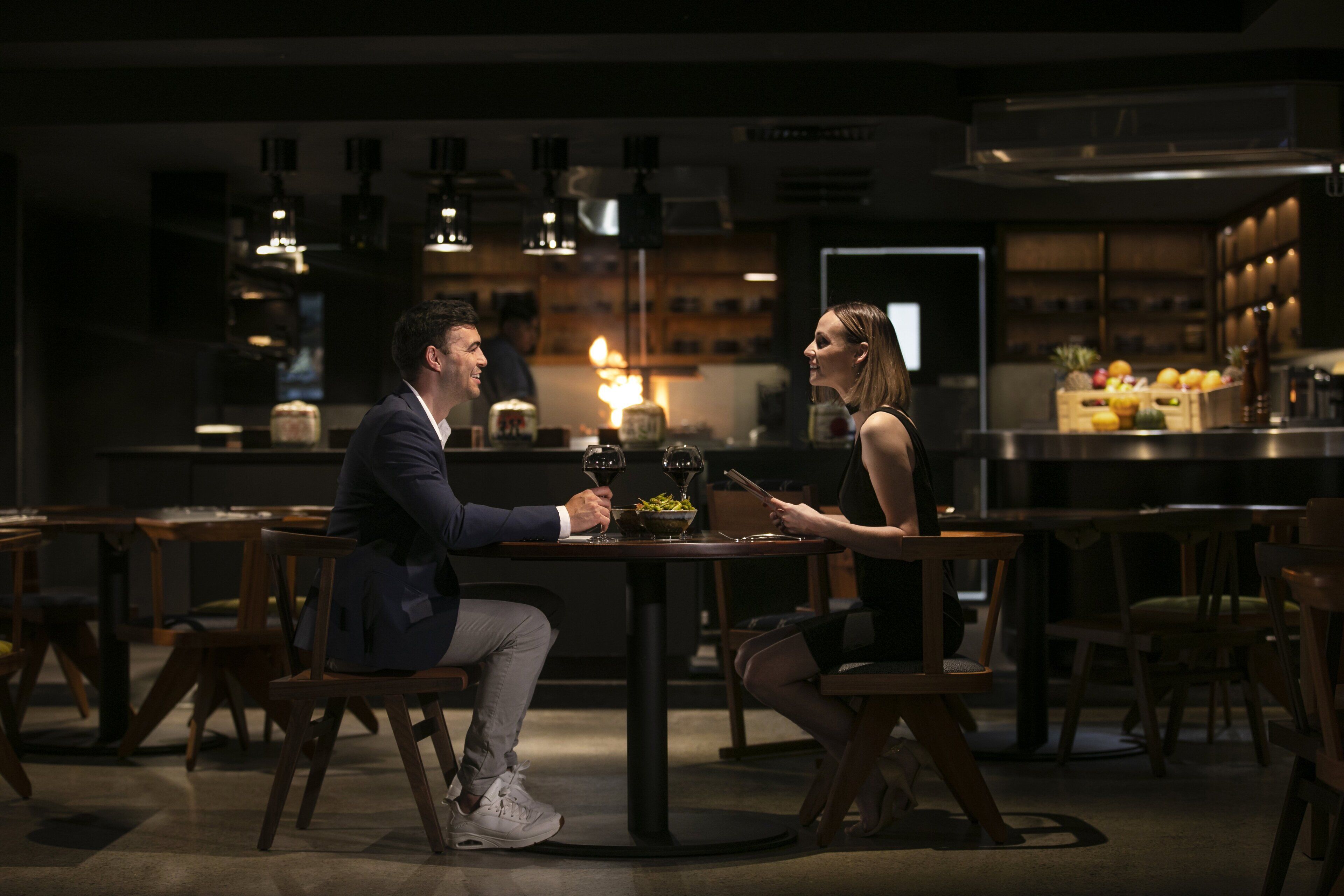 Una pareja cenando en un restaurante con poca luz, muebles de madera e iluminación colgante.
