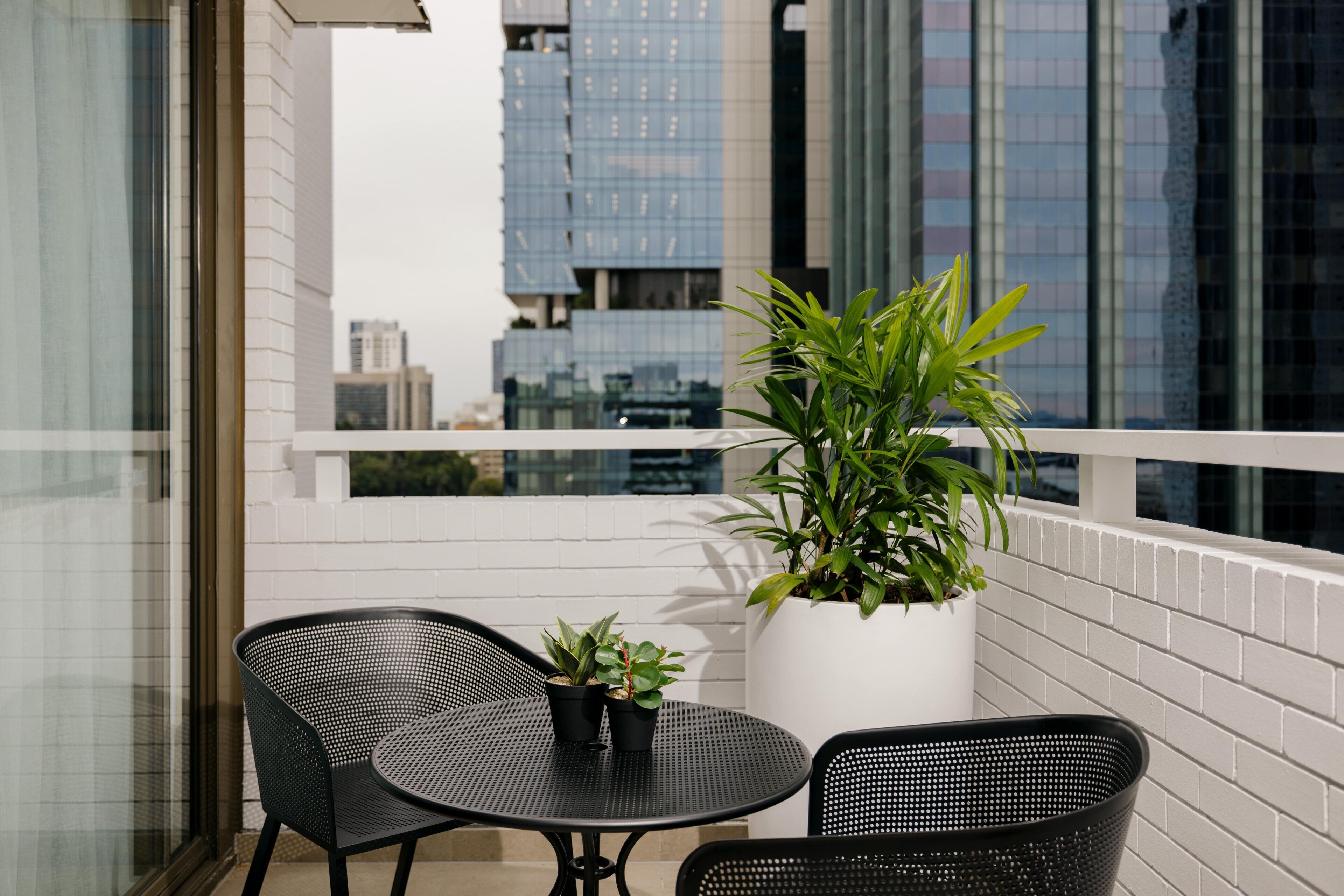 A balcony with two black metal chairs and a round table, a potted plant, and a white brick wall.