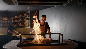Un cocinero preparando comida sobre una parrilla a fuego en una cocina.