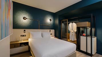 A modern hotel room with a large bed, a bedside table, a wardrobe, and a wall-mounted light fixture.