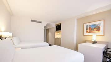 Quarto de hotel com duas camas, uma escrivaninha, uma cadeira, um quadro na parede e um abajur.