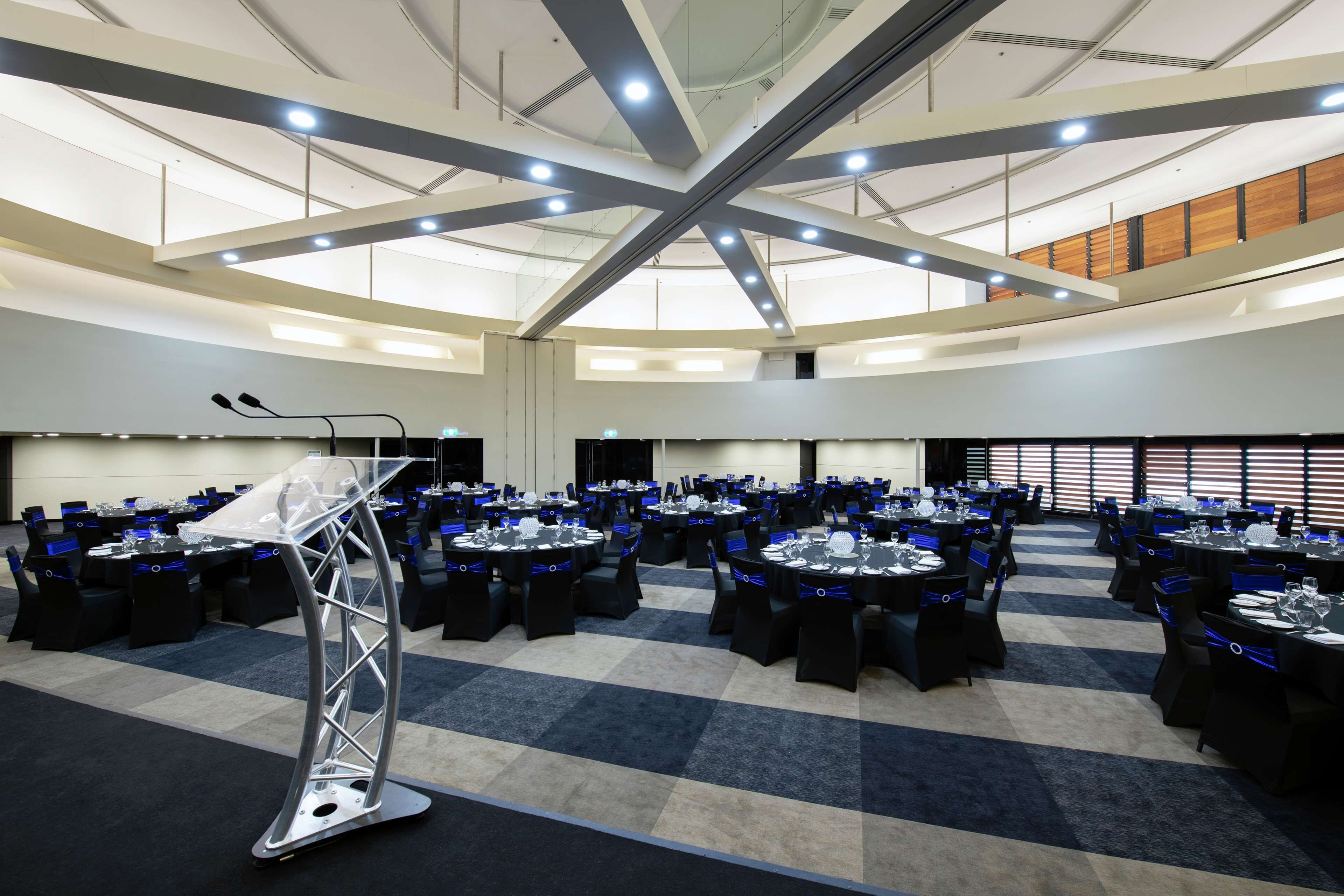 A conference room with multiple tables, a podium, and a high ceiling with lighting fixtures.