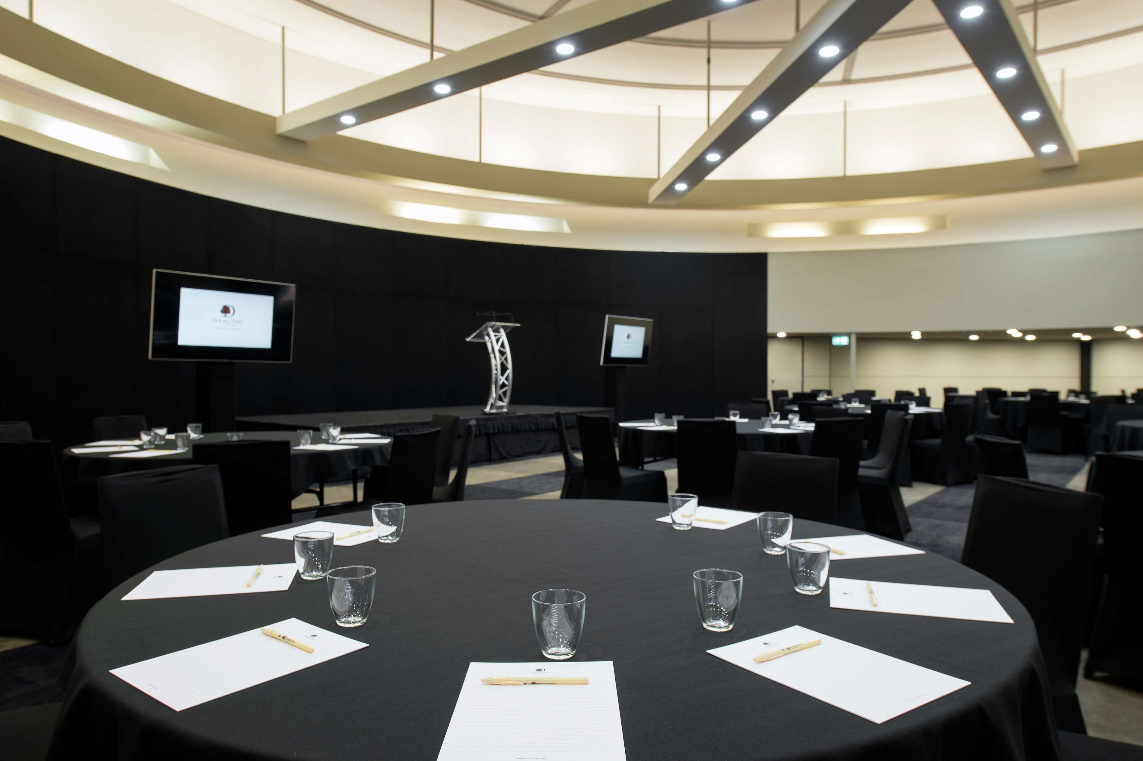 A conference room with a large round table, multiple chairs, and a high ceiling with lighting fixtures.