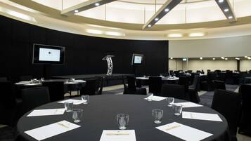 Una sala de conferencias con una gran mesa redonda, varias sillas y un techo alto con luminarias.