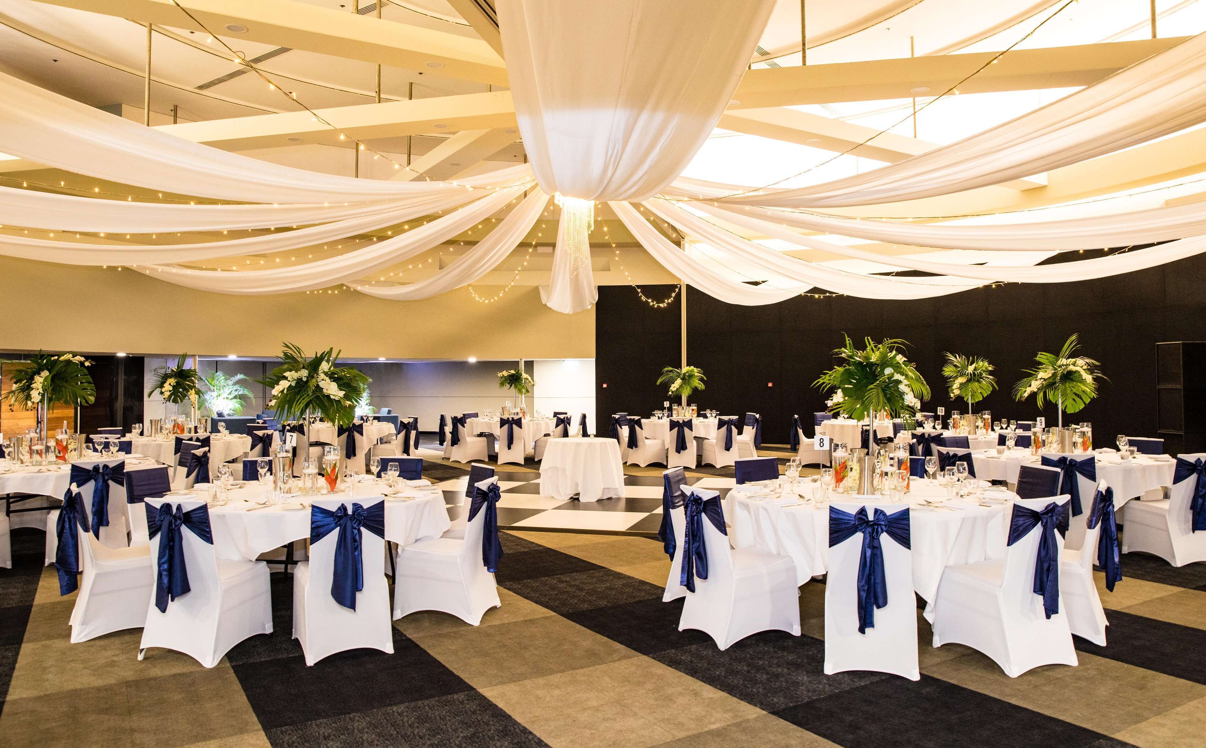 A banquet hall with tables set for a formal event, featuring white tablecloths and blue sashes.