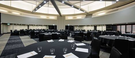 A conference room with multiple tables, each with papers and glasses, in a modern building with a high ceiling and natural light.
