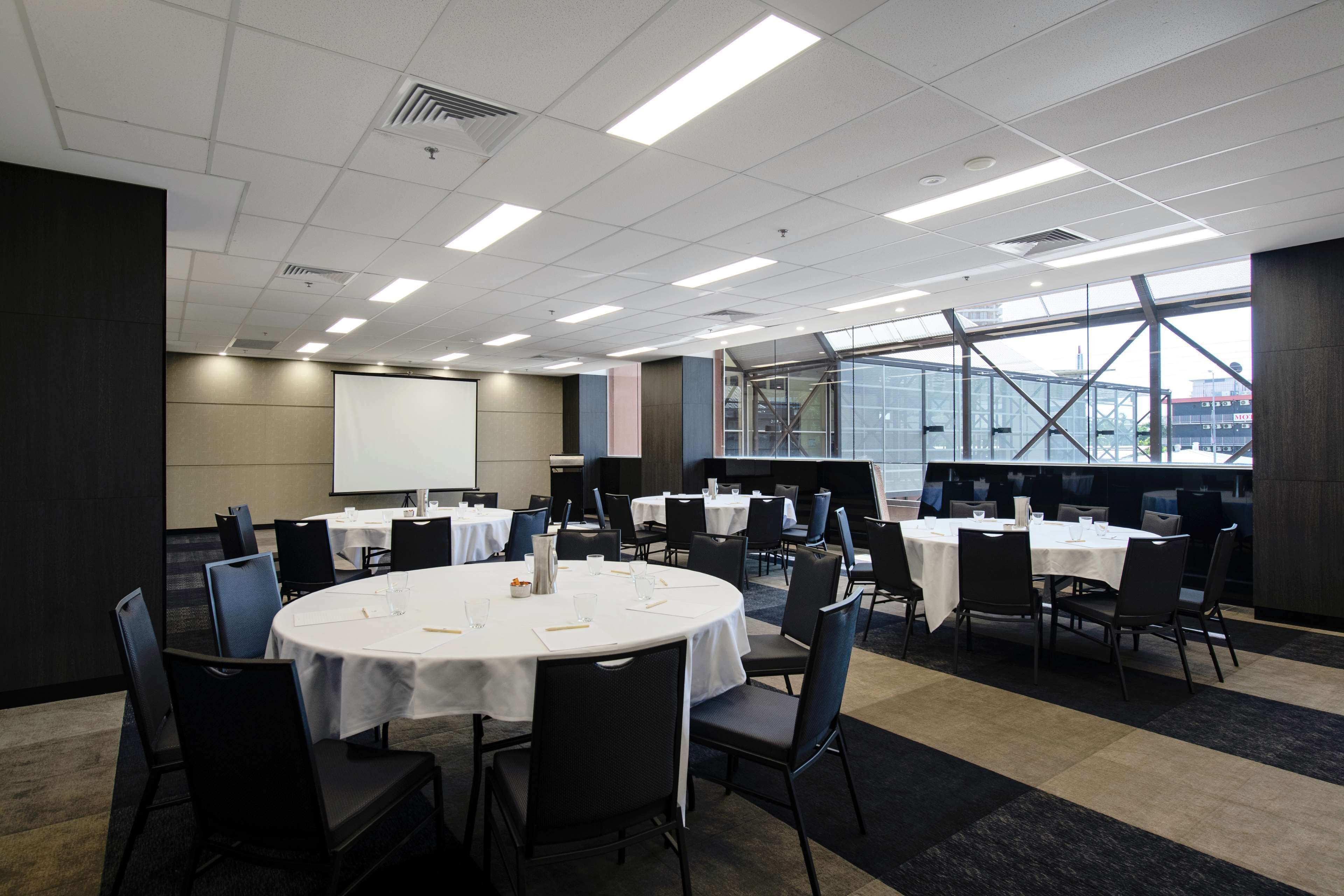A conference room with multiple tables and chairs, a whiteboard, and large windows offering a view of the city.