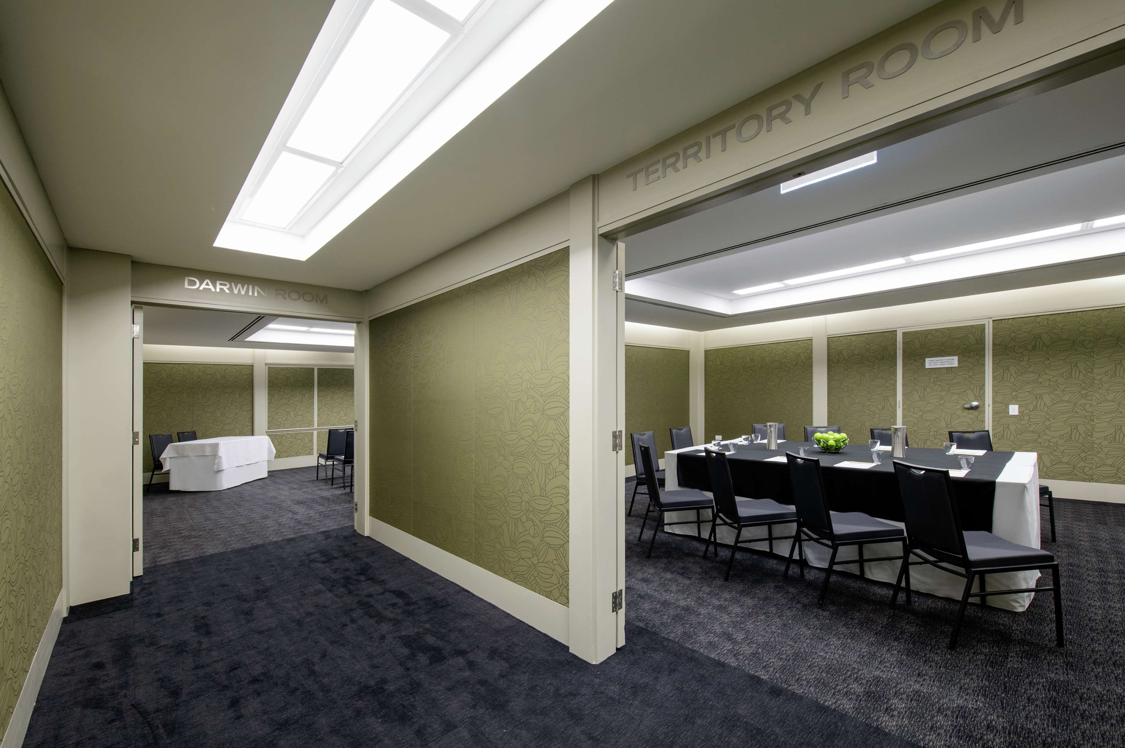A conference room with a long table, chairs, and a white tablecloth. There is a sign above the door labeled "Darwin Room."