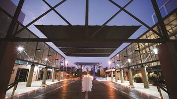 A covered outdoor area with a table set for a wedding ceremony, surrounded by pillars and lights.