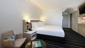 A hotel room with a bed, a chair, a nightstand, a lamp, and a television.