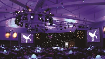 A conference room with a stage, multiple screens, and a ceiling with lighting fixtures.
