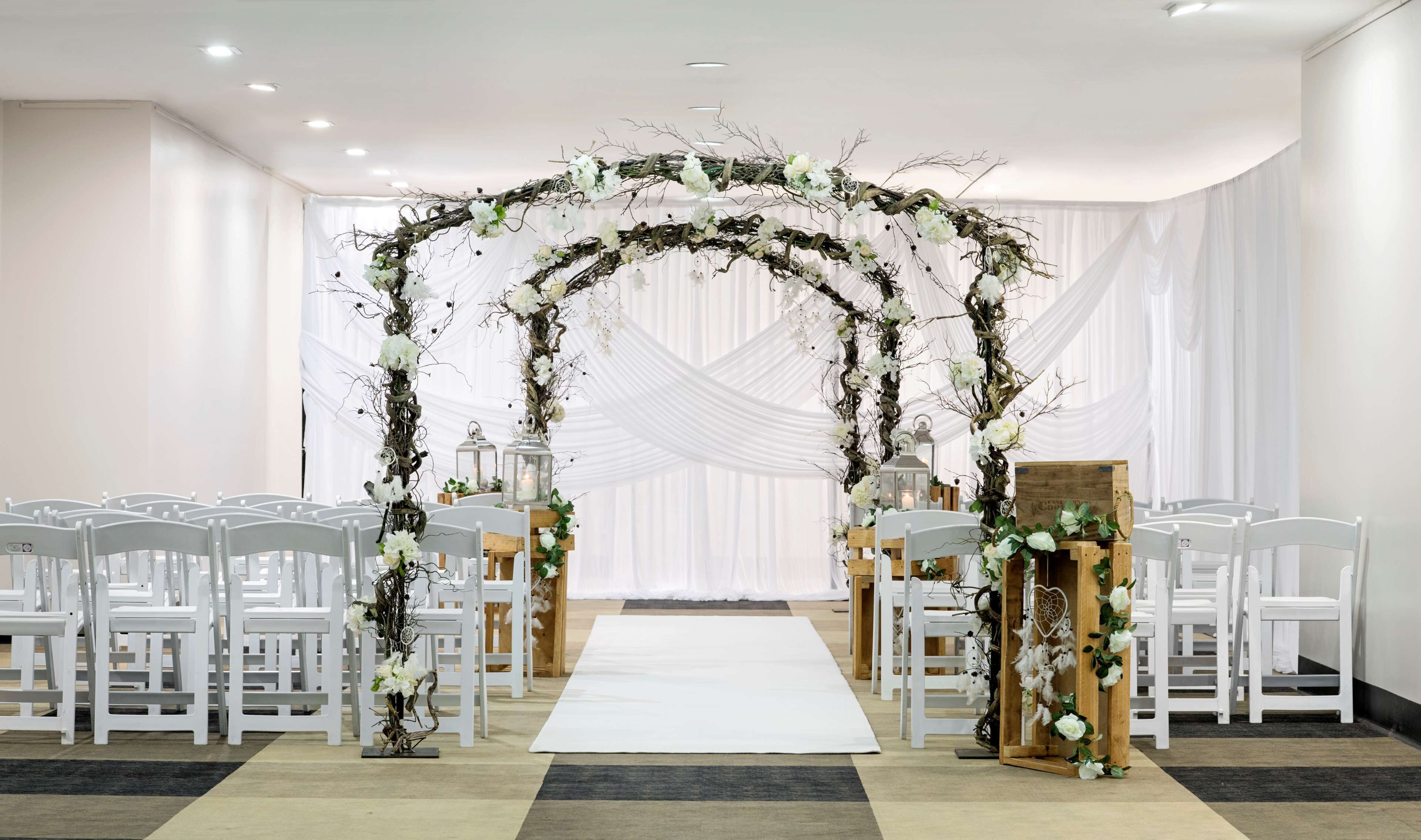 A wedding ceremony setup with white chairs, a white aisle, and a floral arch.