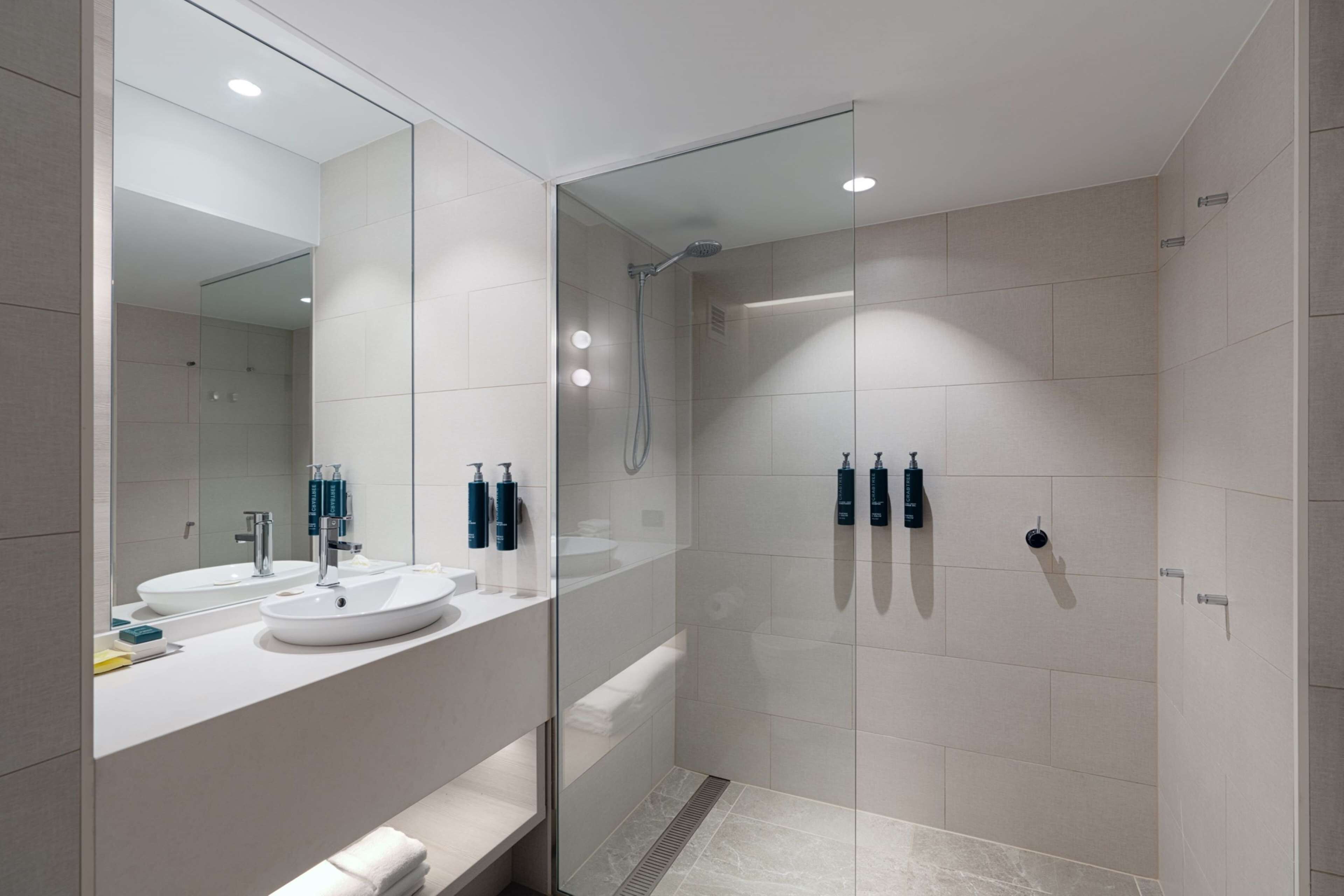 A modern bathroom with a glass-enclosed shower, a large mirror, and two sinks.