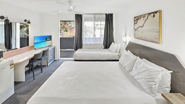 A hotel room with a large bed, a desk with a computer, a TV, and a balcony with curtains.