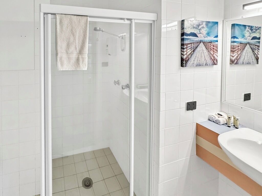 A modern bathroom with a glass-enclosed shower, white tiles, and artwork on the walls.