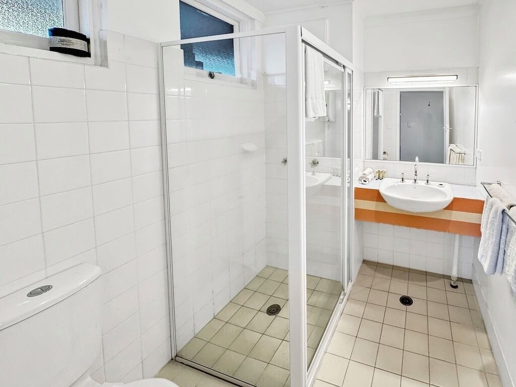 A modern bathroom with a glass-enclosed shower, a white sink, and a large mirror.