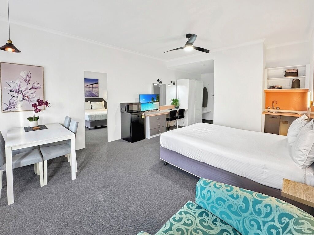 Ett modernt hotellrum med en säng, ett skrivbord, en stol, en tv och en takfläkt.