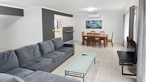 A modern living room with a grey sofa, a glass-top coffee table, and a dining area with wooden chairs and a table.