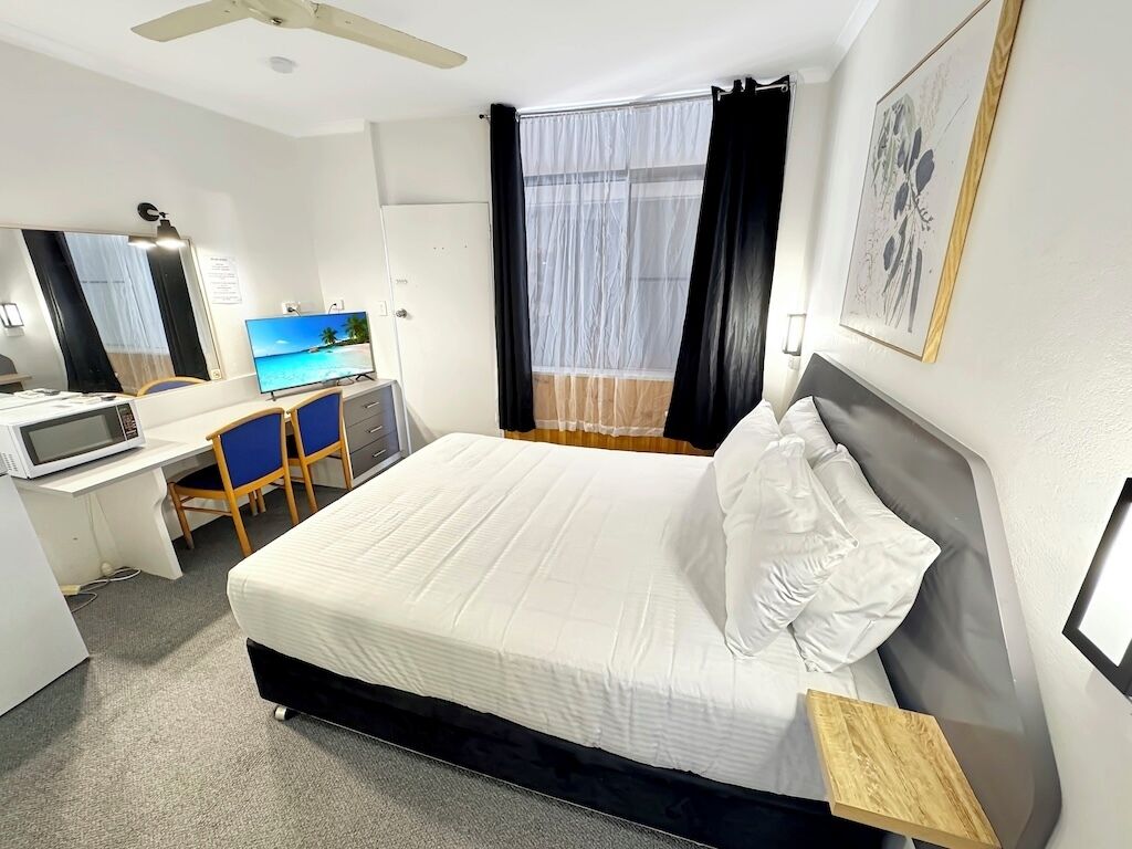 A hotel room with a bed, a desk with a computer, a TV, and a window with curtains.