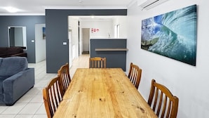 A modern dining area with a wooden table and chairs, a grey sofa, and a kitchen area in the background.