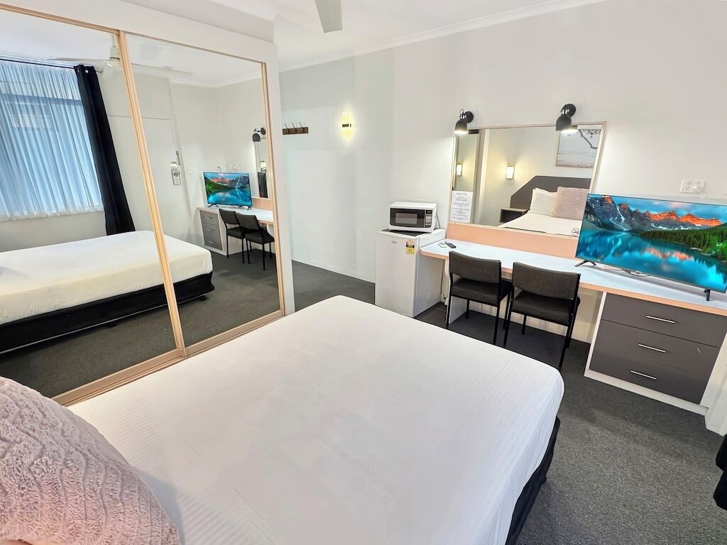 A hotel room with a bed, a desk with a computer, a TV, and a mirror.