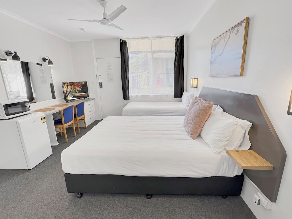 A hotel room with a bed, desk, chair, TV, and a window with curtains.